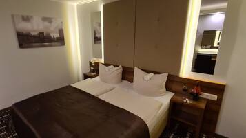 Habitación de hotel con una cama grande, una mesita de noche con lámpara, un espejo y un cuadro en la pared.