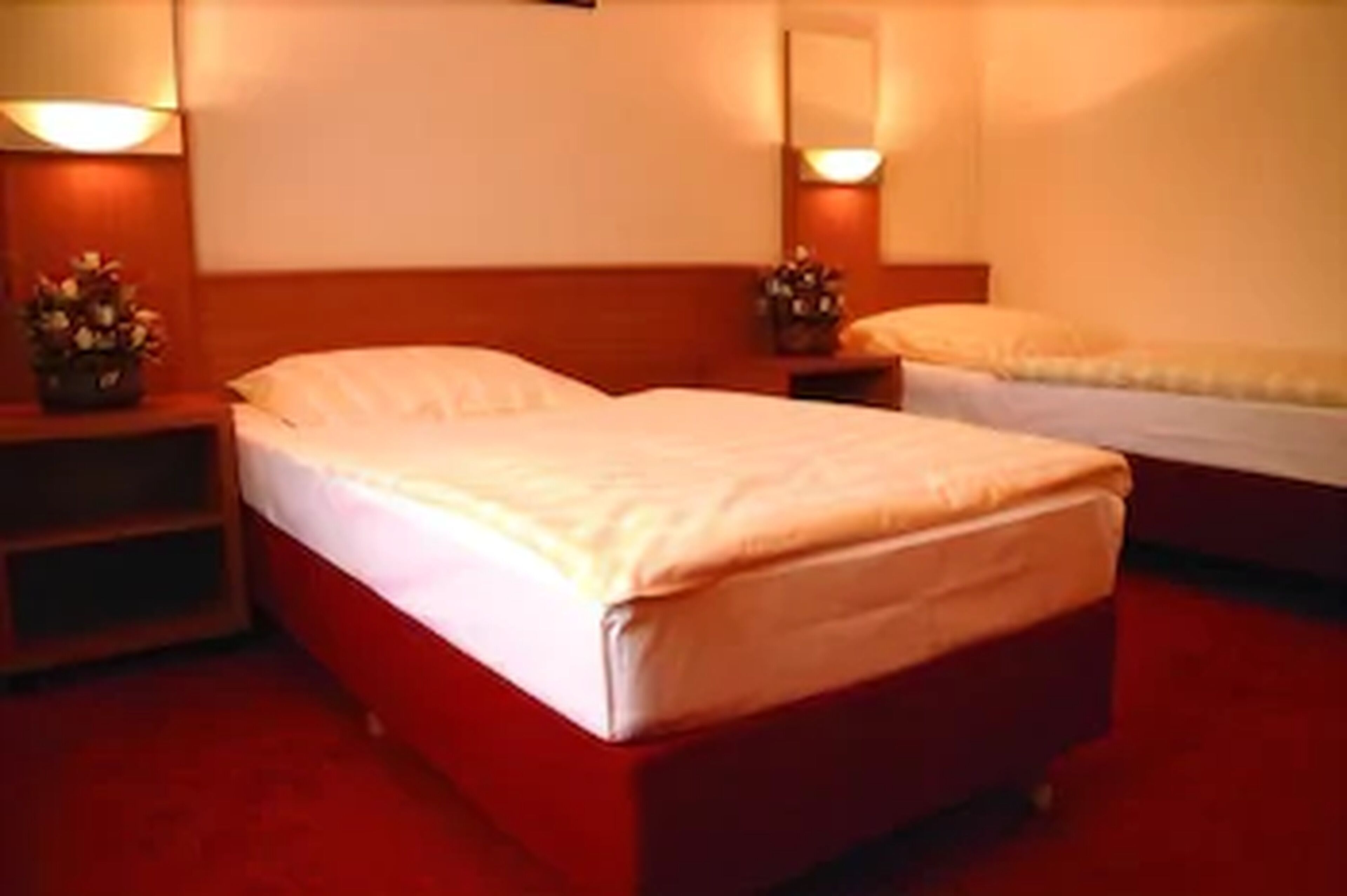 Une chambre d’hôtel avec deux lits, chacun doté d’une tête de lit en bois et d’une table de chevet avec une lampe et un vase à fleurs.