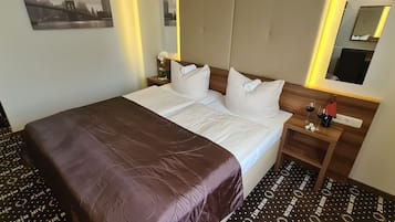 A hotel room with a large bed, a nightstand with a lamp, a mirror, and a small table with a wine glass.