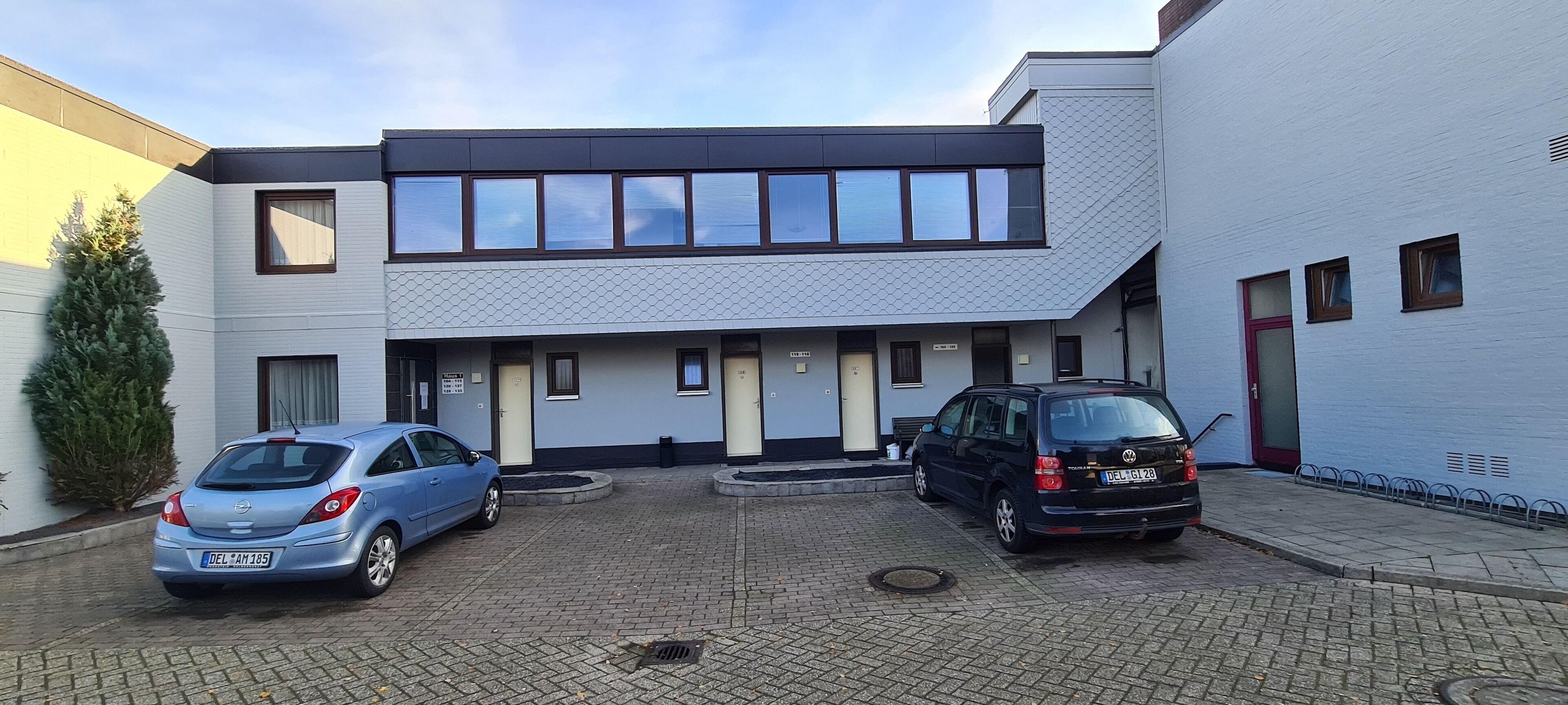 A modern building with a flat roof, multiple windows, and a paved courtyard.