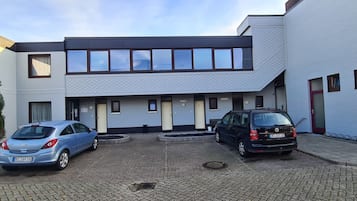 A modern building with a flat roof, multiple windows, and a paved courtyard.
