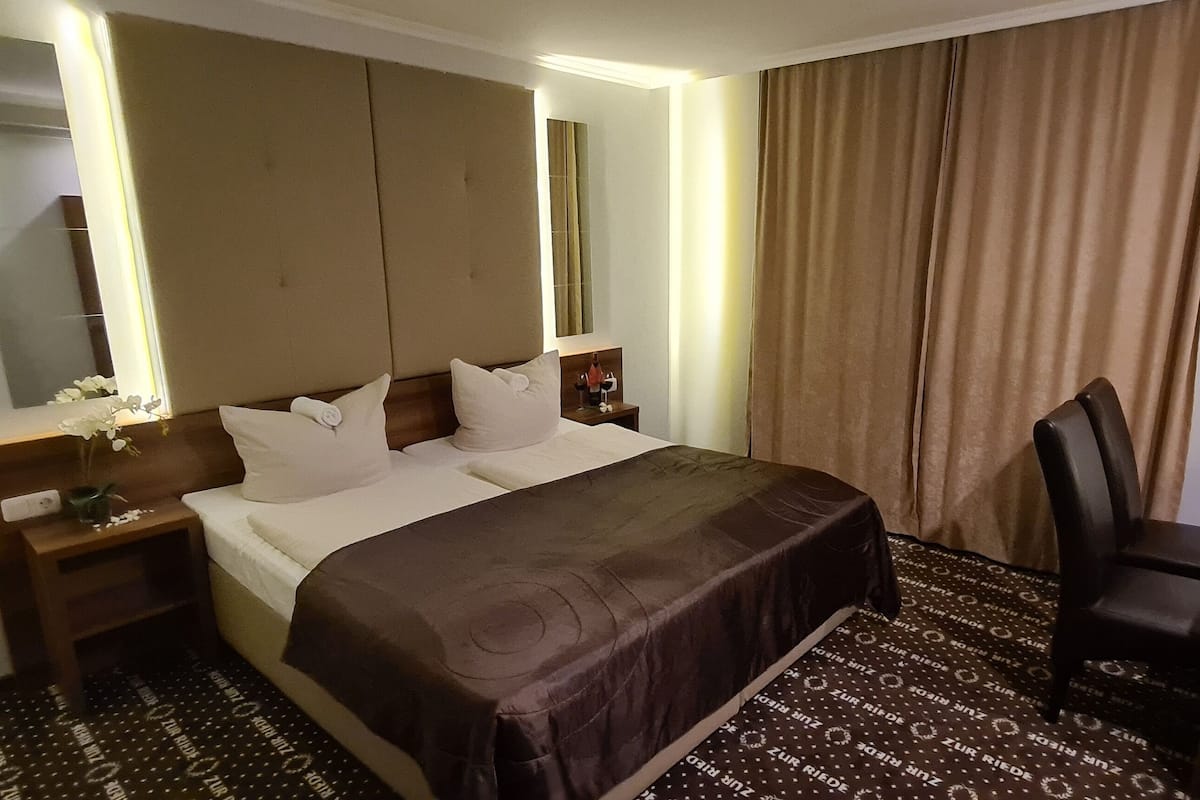 A hotel room with a large bed, a desk, a chair, a mirror, and a wardrobe.