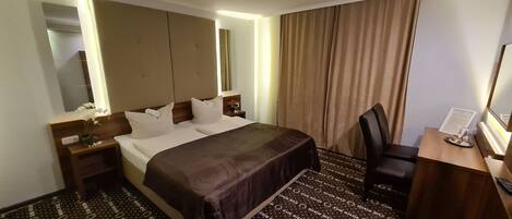 Une chambre d’hôtel avec un grand lit, un bureau, une chaise, un miroir et une armoire.
