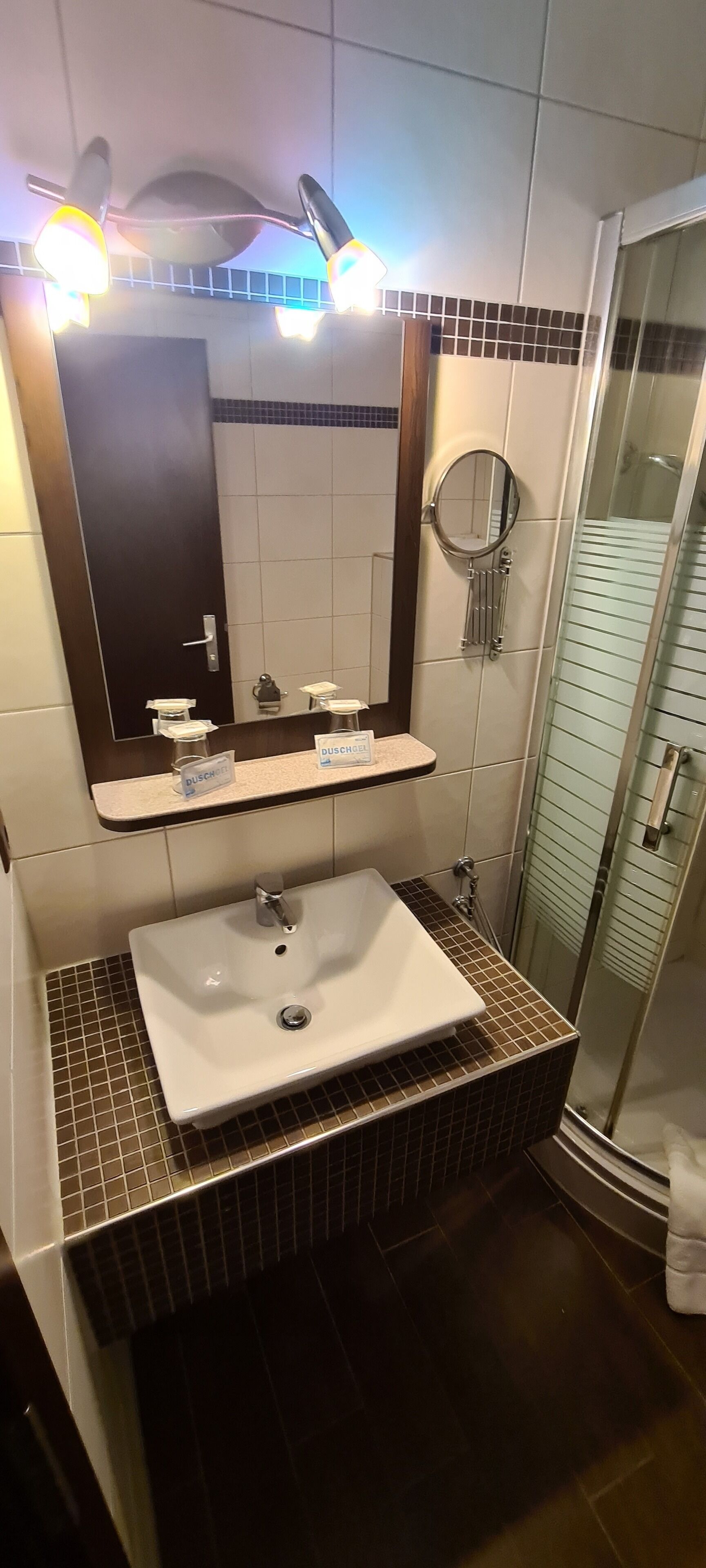 Ein Badezimmer mit einem weißen Waschbecken, einem Spiegel und einer Duschkabine aus Glas.