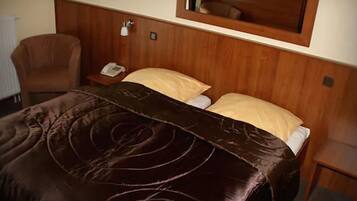 A hotel room with a wooden headboard, a brown leather bedspread, a bedside table with a telephone, and a chair.