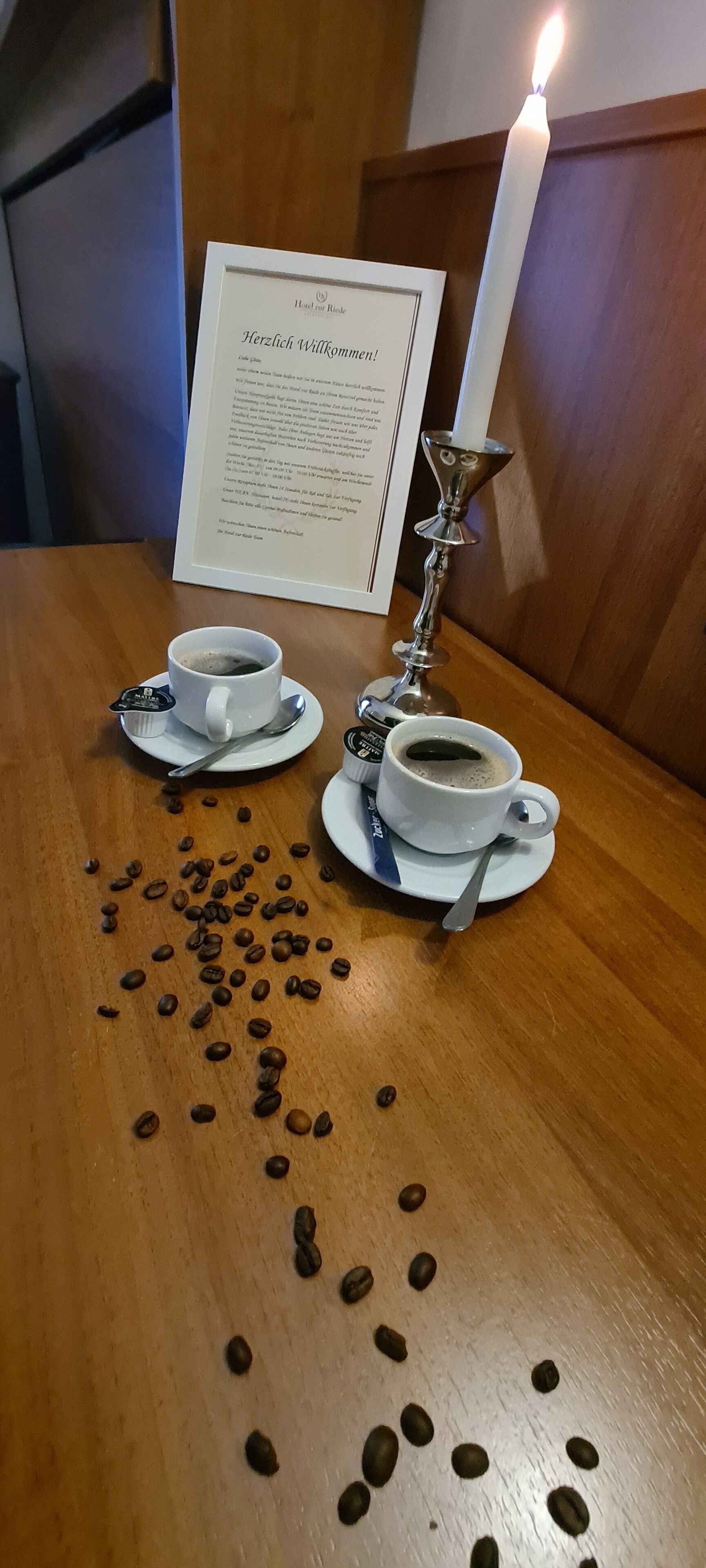 Two white cups of coffee on saucers with a menu sign and a lit candle in the background.