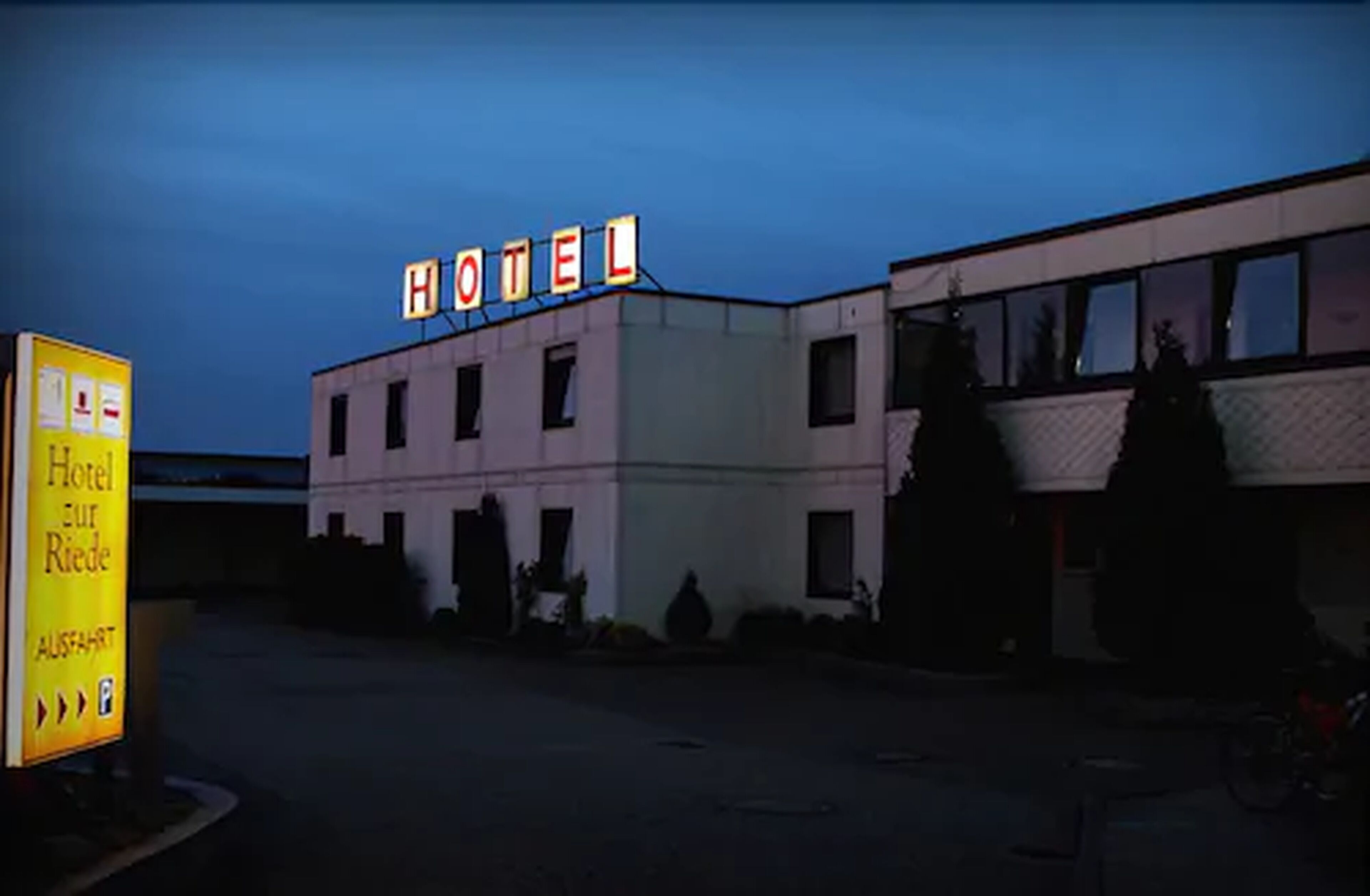 A building with a sign reading "HOTEL" and a sign on the left indicating "Hotel zur Riede" with parking.
