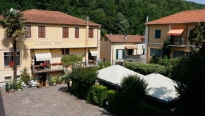 A building named 'Albergo Amici' with a tiled roof, a balcony with flowers, and a garden area with potted plants and outdoor seating. - Albergo Amici (Varese Ligure)