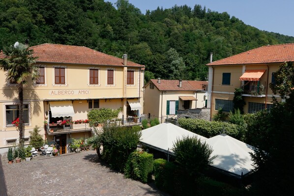 A building named 'Albergo Amici' with a tiled roof, a balcony with flowers, and a garden area with potted plants and outdoor seating.