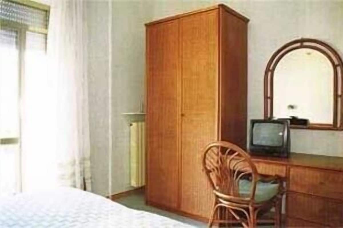 Un dormitorio con un armario de madera, una silla, un escritorio con televisor y una cama.