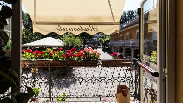 A balcony with a wrought iron railing, potted plants, and a large beige awning with the word "Cappuccino" on it. - Albergo Amici (Varese Ligure)