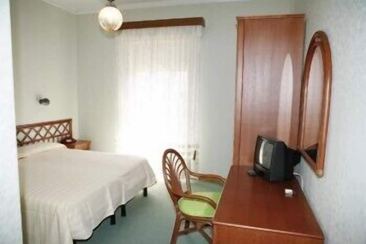 Habitación de hotel con cama, un escritorio de madera con televisor, una silla y un espejo grande.