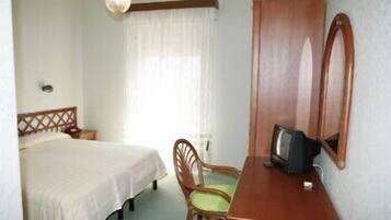 A hotel room with a bed, a wooden desk with a television, a chair, and a large mirror.