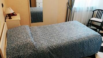 Una habitación con cama, una silla, una mesita de noche con lámpara y un espejo.