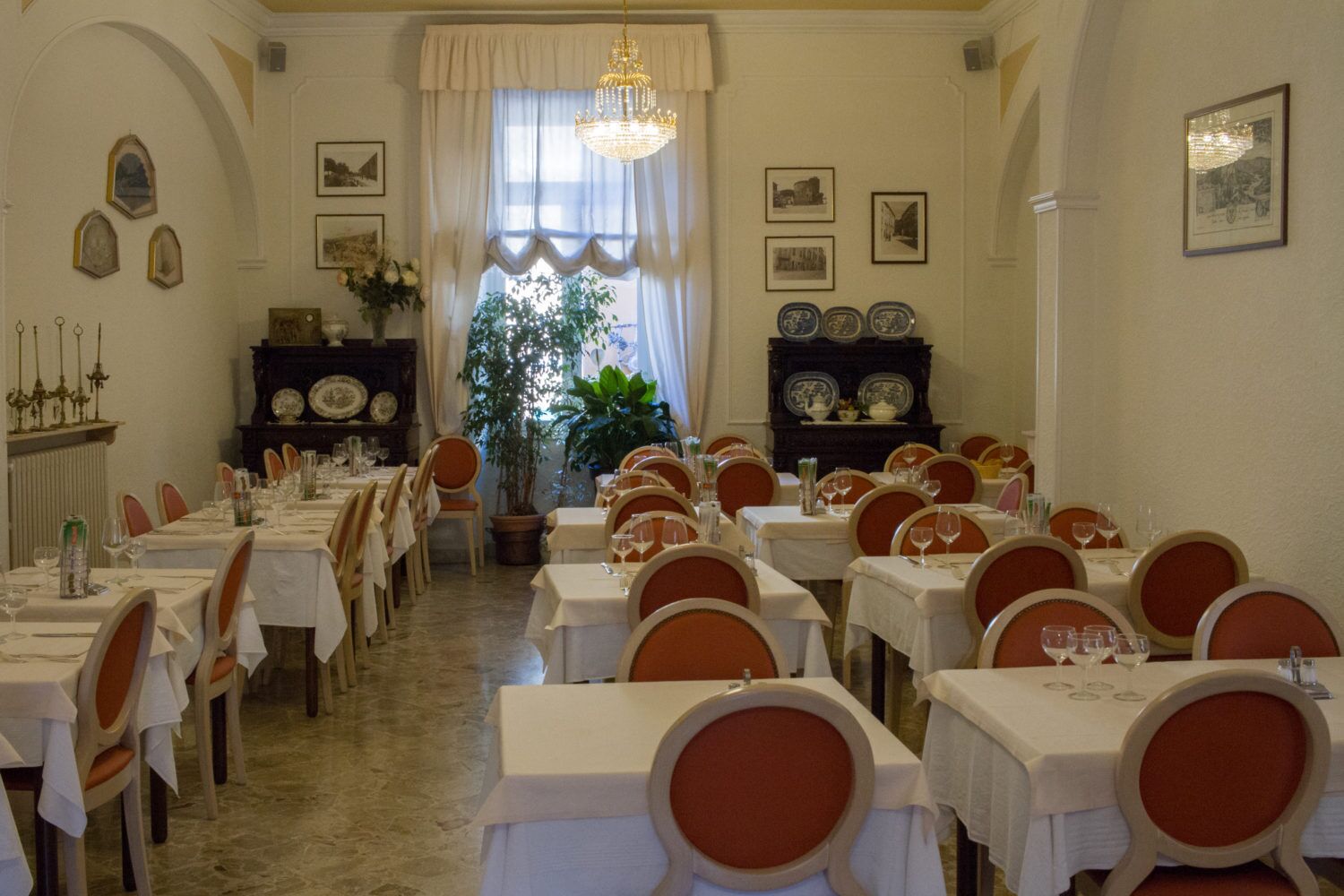 Un comedor con varias mesas y sillas, un candelabro y cuadros en las paredes.