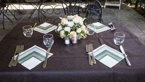 A table set for a meal with a dark tablecloth, white napkins with green patterns, and a centerpiece of flowers. - Albergo Amici (Varese Ligure)