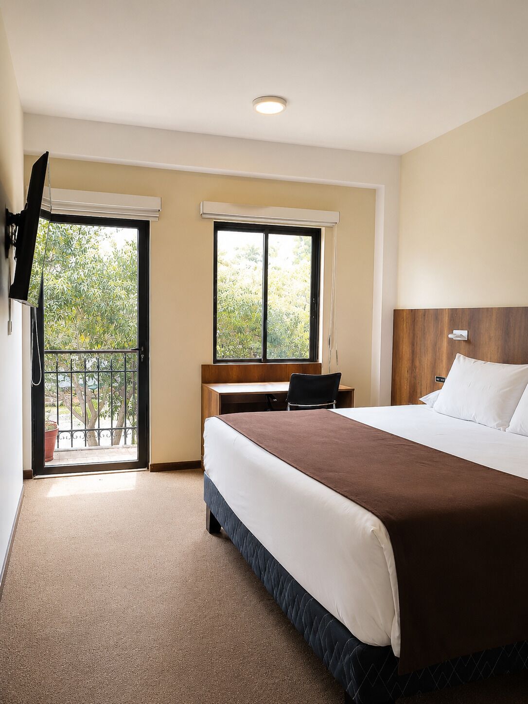 A hotel room with a bed, desk, and a TV mounted on the wall.