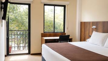 A hotel room with a bed, desk, and a TV mounted on the wall.