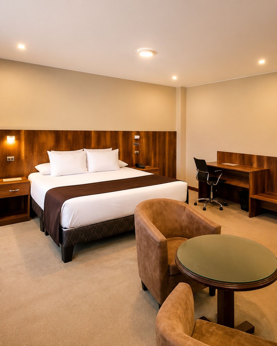 Habitación de hotel con cama, escritorio, dos sillas y una mesita.