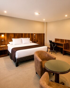 Habitación de hotel con cama, escritorio, dos sillas y una mesita.
