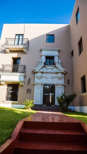 Un edificio con una entrada central, un pequeño balcón y una escalera que conduce a la entrada.