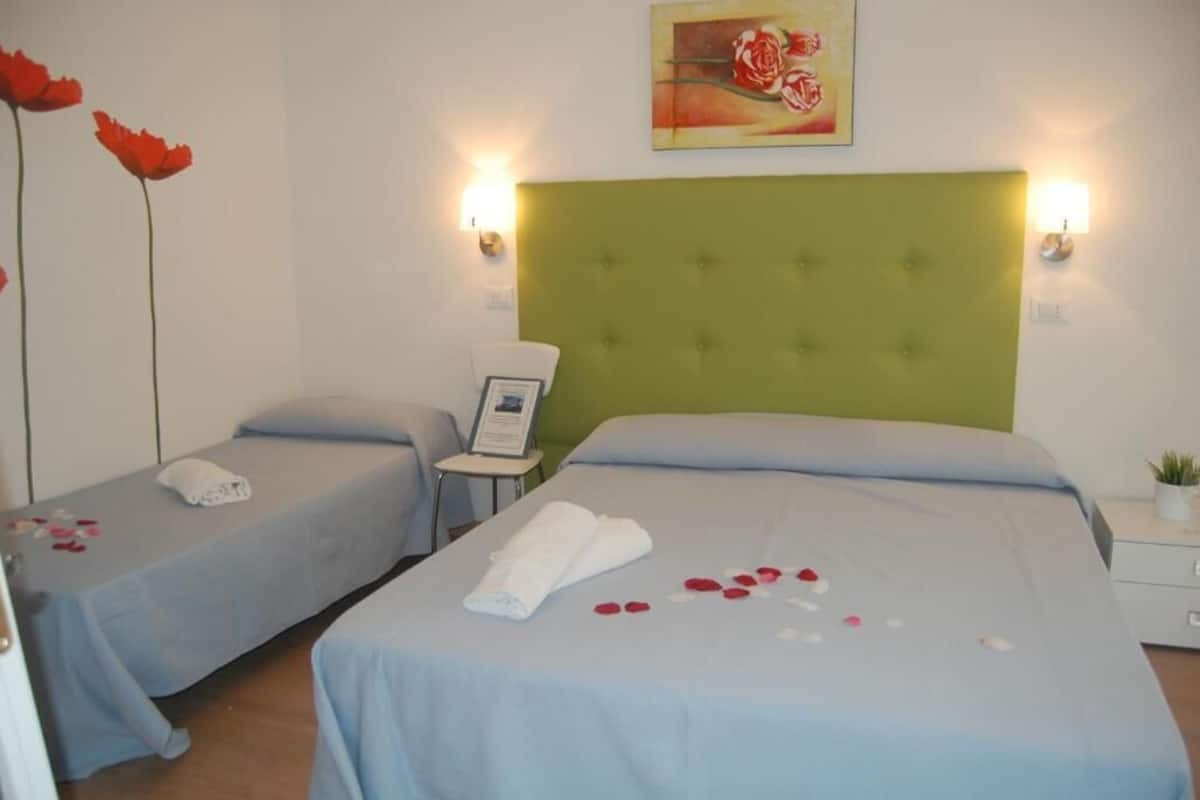 A hotel room with two single beds, a green headboard, and a painting on the wall.