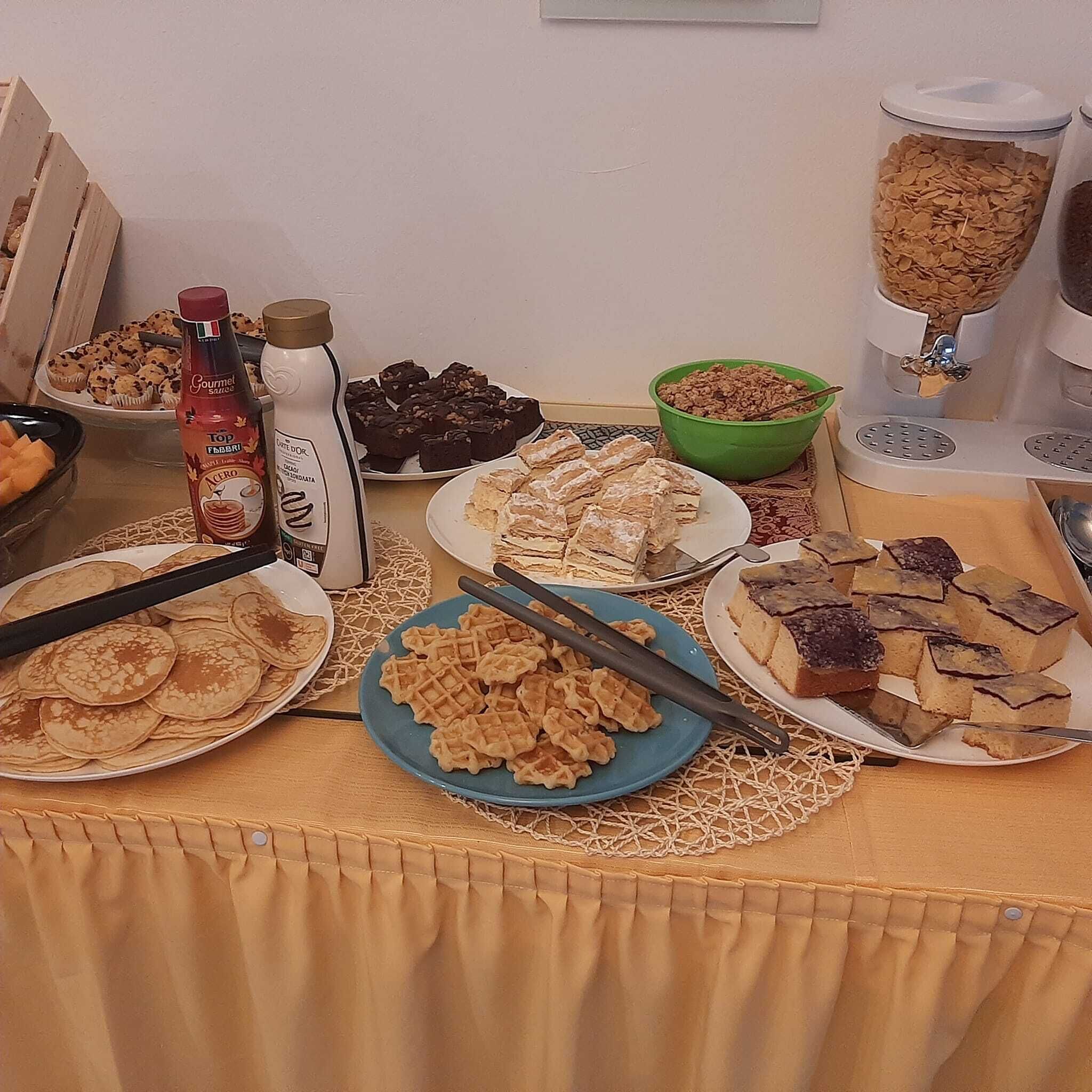 A buffet table with various food items including pancakes, waffles, and desserts.