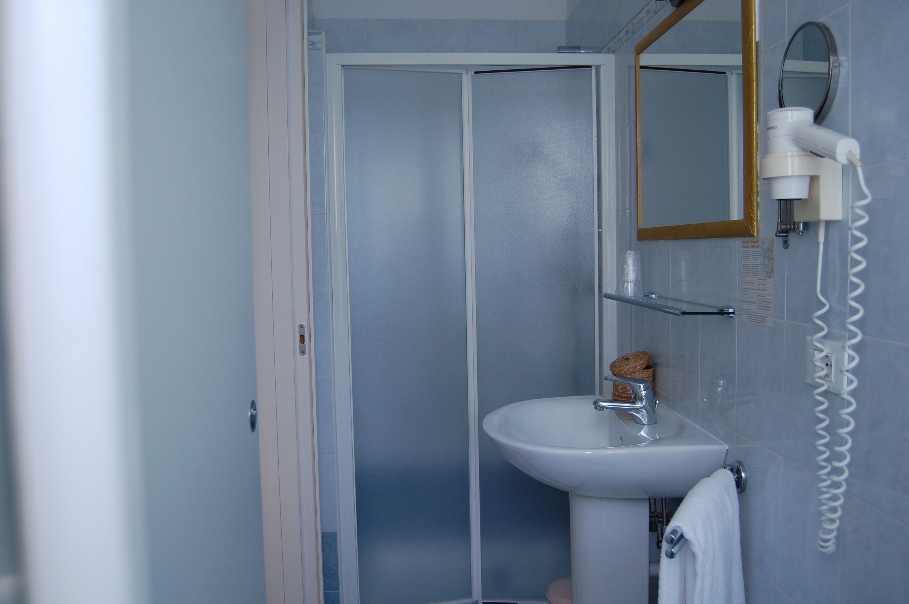 Une salle de bain avec un lavabo blanc, un miroir et un sèche-cheveux fixé au mur.