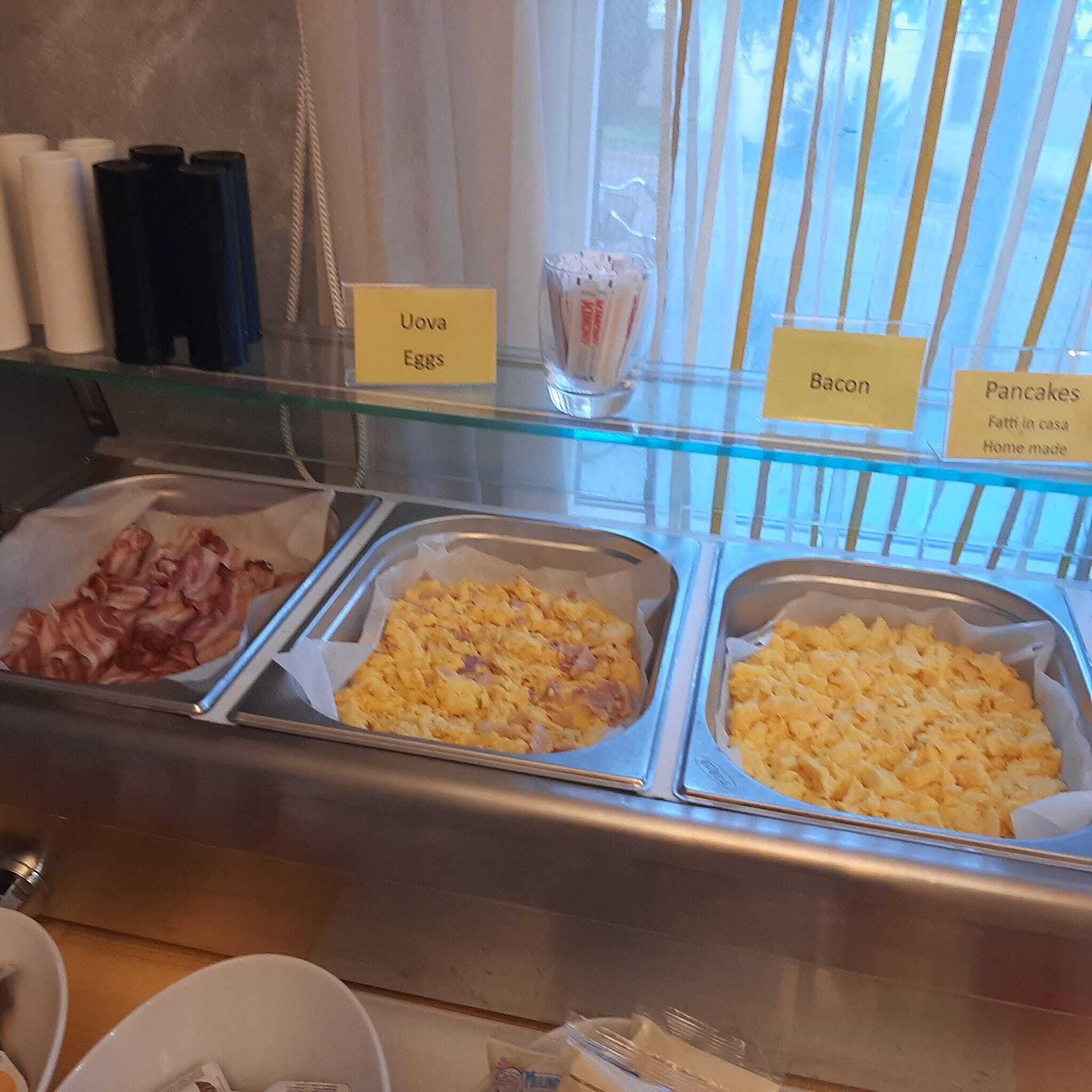 A breakfast buffet with labeled sections for uova eggs, bacon, and pancakes.