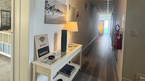 A hallway with a white console table, a WiFi sign, a lamp, and a fire extinguisher. - Hotel Irene (Lignano Sabbiadoro)