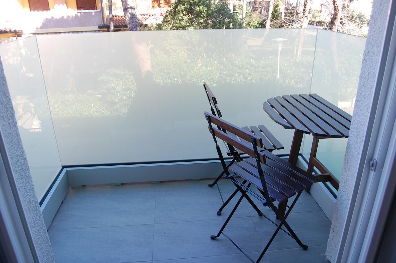 A balcony with a glass partition, a wooden table, and two wooden chairs.