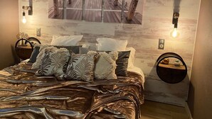 Un dormitorio con una cama, almohadas, una lámpara fijada en la pared y un adorno mural.
