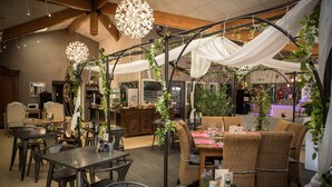 Un restaurante con techos altos, vigas a la vista y plantas colgantes. Las mesas están preparadas con manteles blancos y velas.