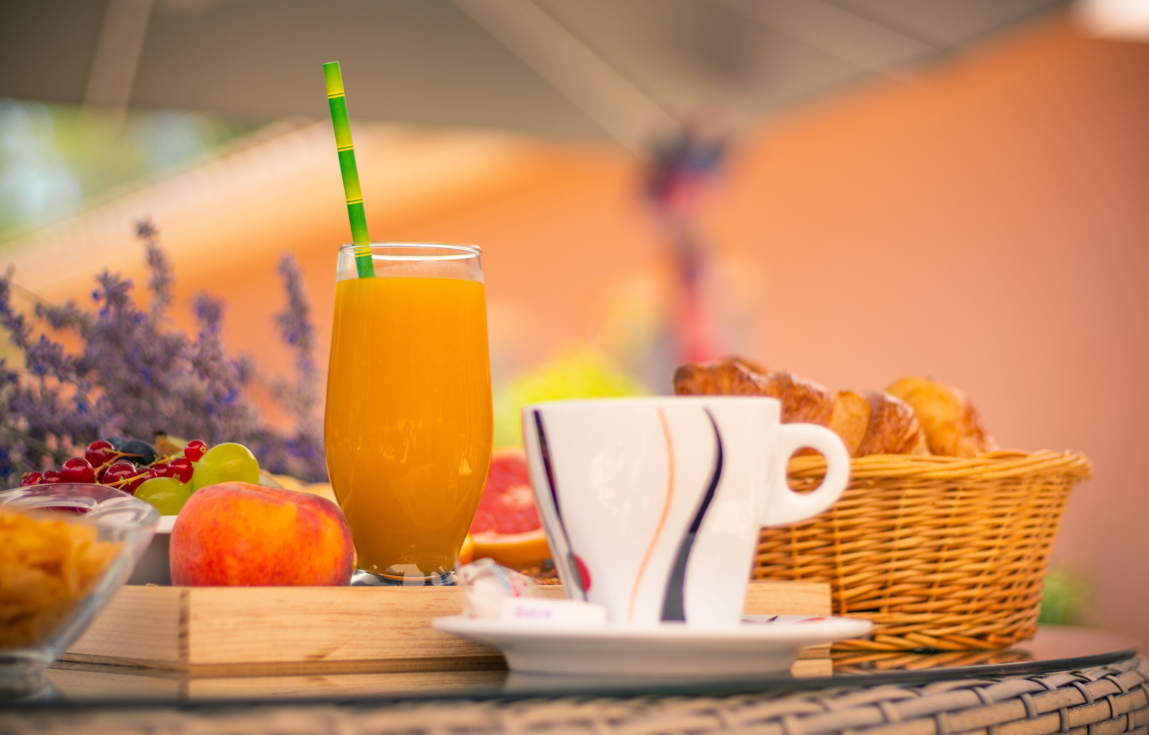 Un desayuno con un vaso de zumo de naranja, una taza y una cesta de bollería sobre una mesa.