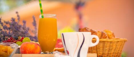 Un desayuno con un vaso de zumo de naranja, una taza y una cesta de bollería sobre una mesa.