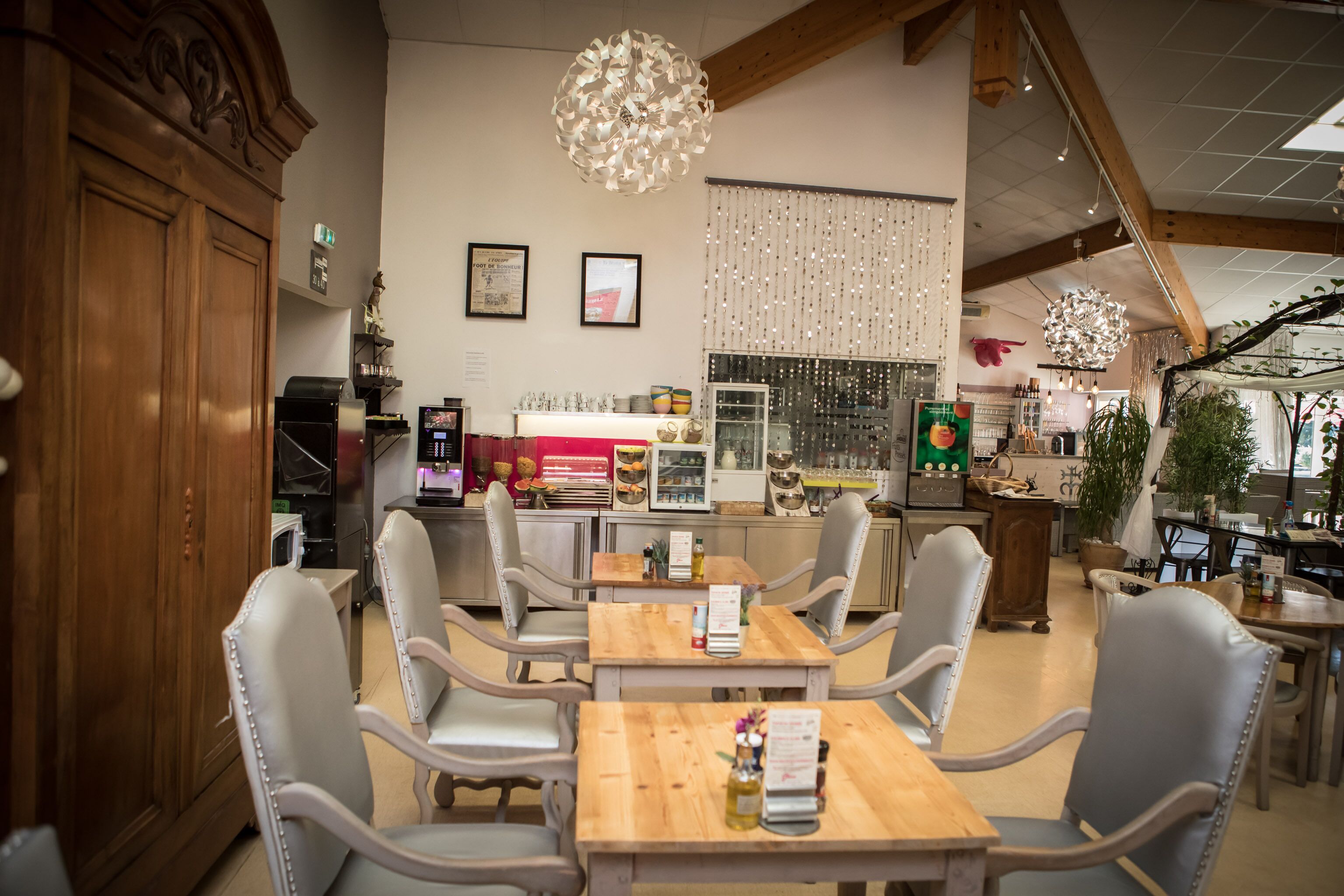 L’intérieur d’un restaurant, avec des tables et des chaises en bois, un appareil à café et un éclairage décoratif.