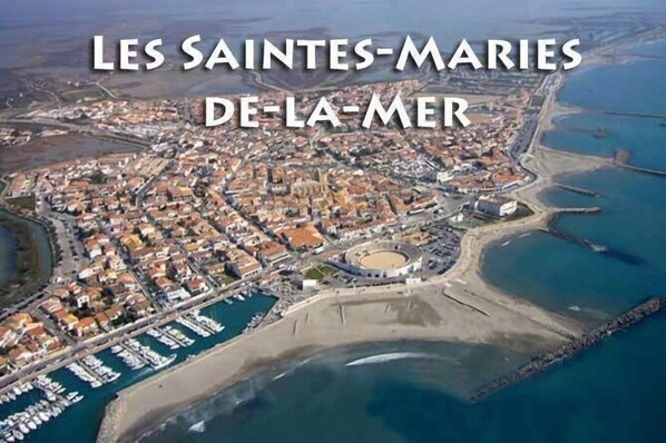 Vista aérea de Les Saintes-Maries de la Mer, mostrando la distribución urbana con edificios, una plaza central y un puerto deportivo.