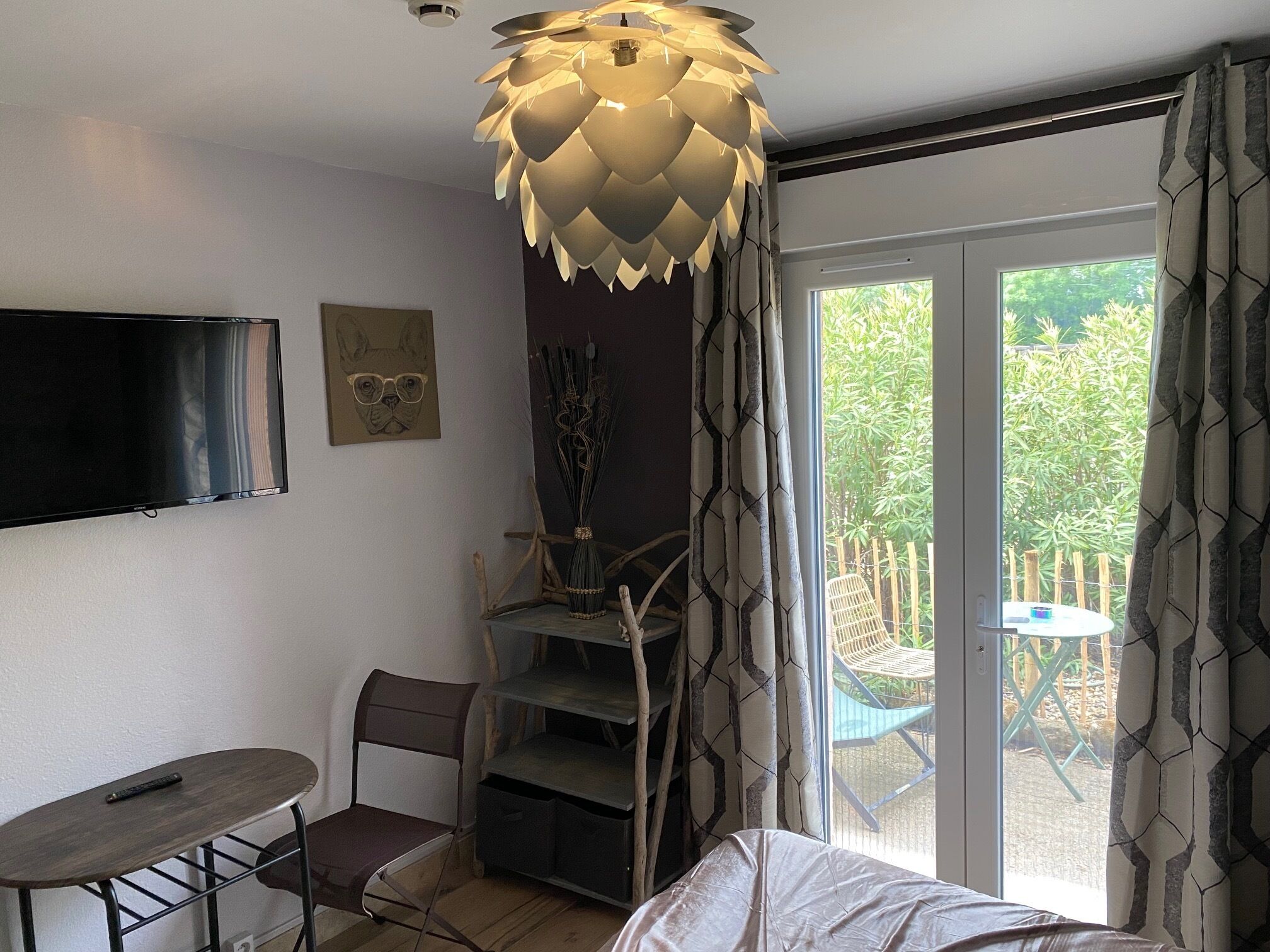 A modern room with a bed, a desk, and a chair. There is a TV mounted on the wall and a window with curtains.