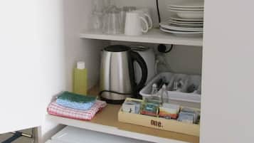 Una kitchenette compacta con microondas, cafetera y refrigerador pequeño.
