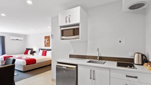Ein kompaktes Hotelzimmer mit Küchenzeile, einem Bett mit rot-weißer Bettwäsche, einem kleinen Esstisch und einem eingebauten Geschirrspüler.