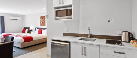 Habitación de hotel pequeña con kitchenette, ropa de cama roja y blanca, una pequeña mesa de comedor y lavavajillas integrado.