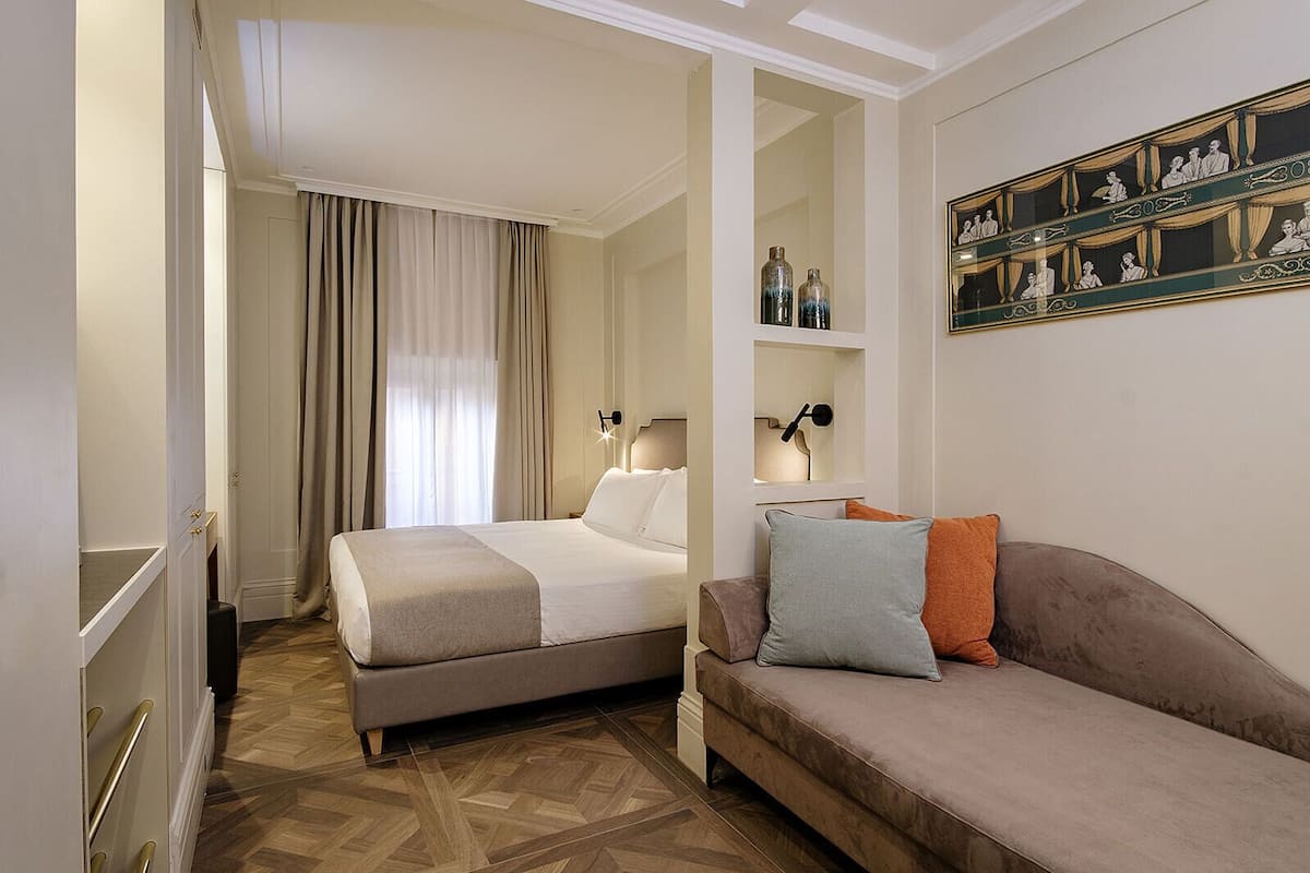 Une chambre d’hôtel comprenant un lit, un canapé, un miroir et une étagère fixée au mur, ornée d’objets décoratifs.