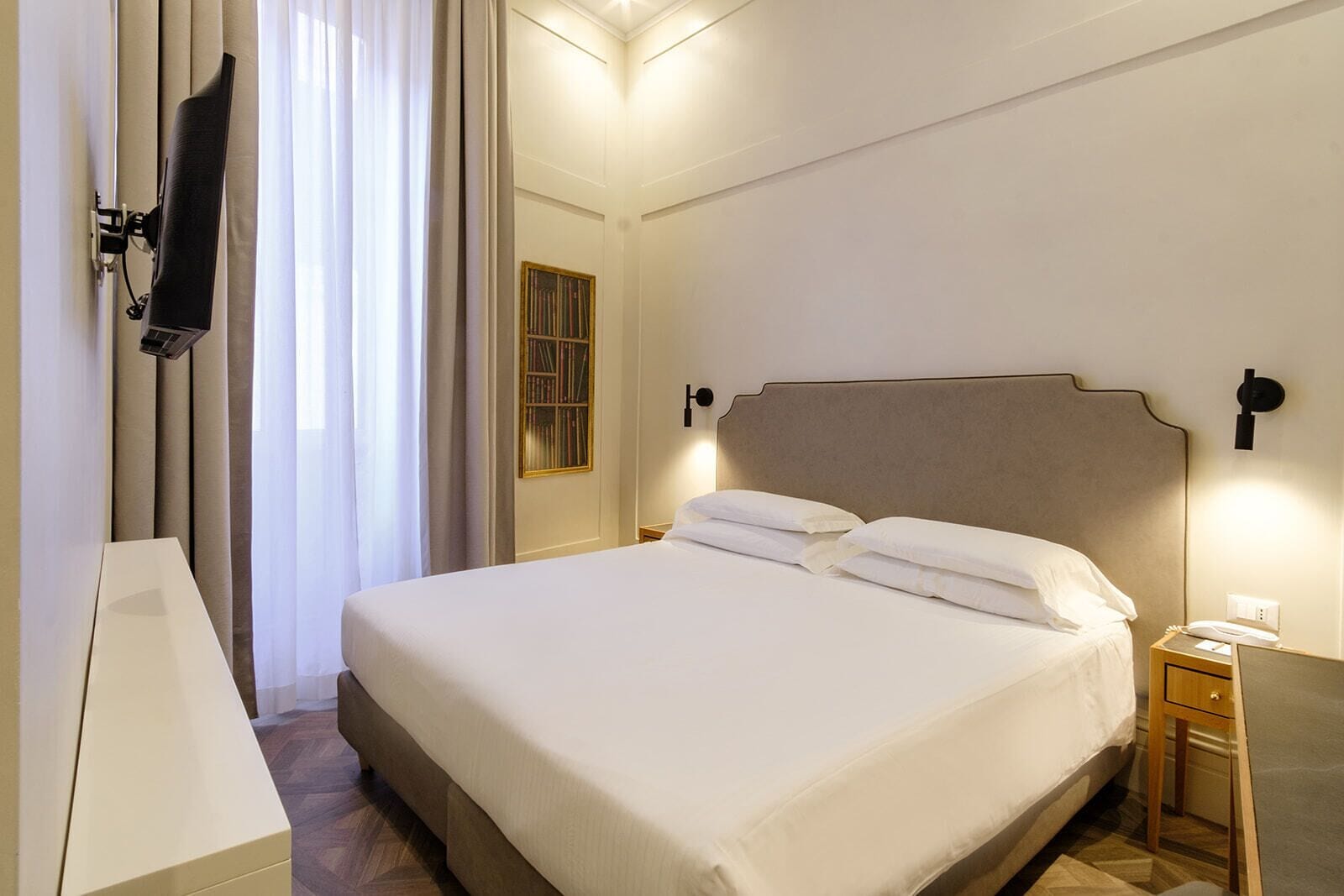 A hotel room with a large bed, bedside tables, a TV mounted on the wall, and a window with curtains.