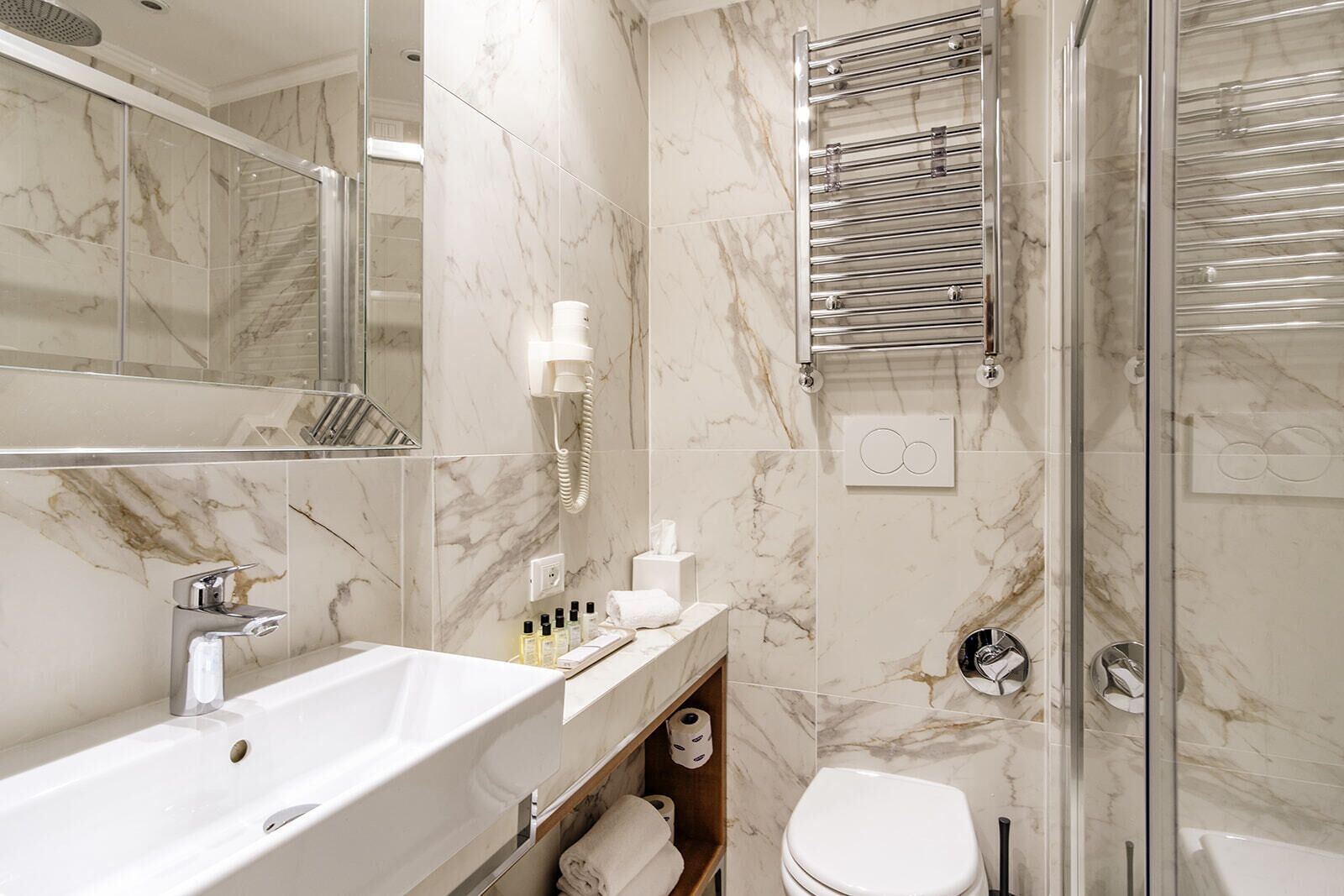 A modern bathroom with a marble backsplash, a glass shower enclosure, a built-in sink, and a towel rack.