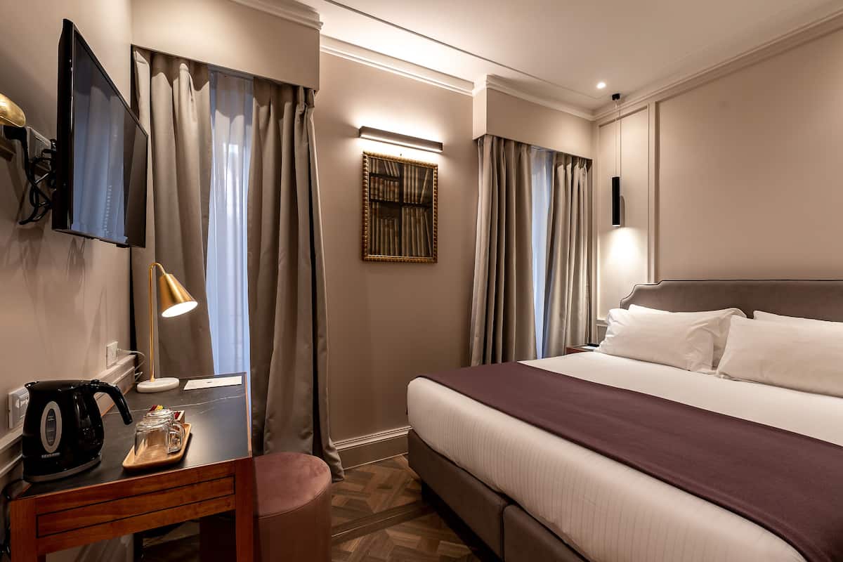 Une chambre d’hôtel comprenant un lit, un bureau avec une bouilloire et un plateau, un téléviseur à écran plat et des rideaux.