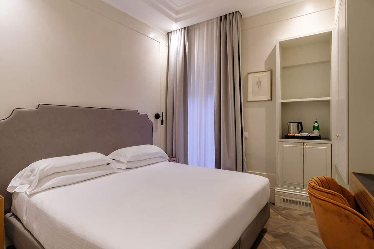 Une chambre d’hôtel comprenant un lit, une armoire, un petit meuble avec un tableau, et une chaise.