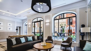 Un moderno vestíbulo de hotel con piso a cuadros, un sofá de cuero negro, una mesa redonda de madera con velas y grandes ventanales con vista a la calle.