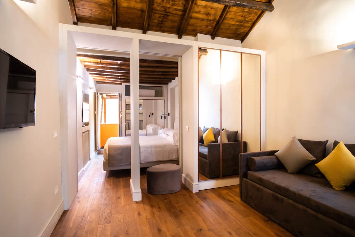 Une chambre d’hôtel moderne avec un plafond en bois, un lit, un canapé et un petit pouf.