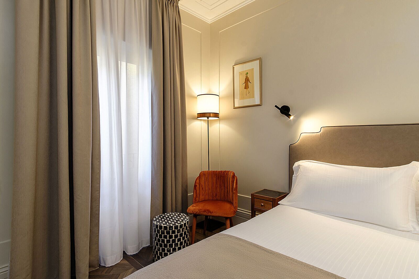 A hotel room with a bed, a chair, a nightstand, a lamp, and a picture on the wall.
