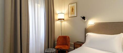 A hotel room with a bed, a chair, a nightstand, a lamp, and a picture on the wall.